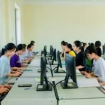 A group of students focusing on computers during a class in a university setting, working indoors.