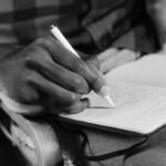 A close-up black and white image of a person writing in a notebook, capturing the essence of expression.
