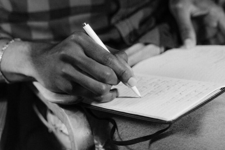 A close-up black and white image of a person writing in a notebook, capturing the essence of expression.