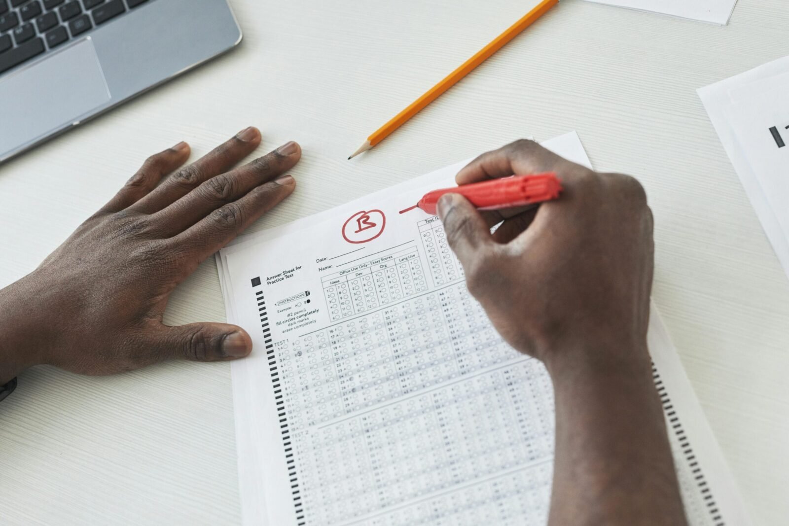 Close-up of a teacher grading multiple choice exams with a red pen on a desk.